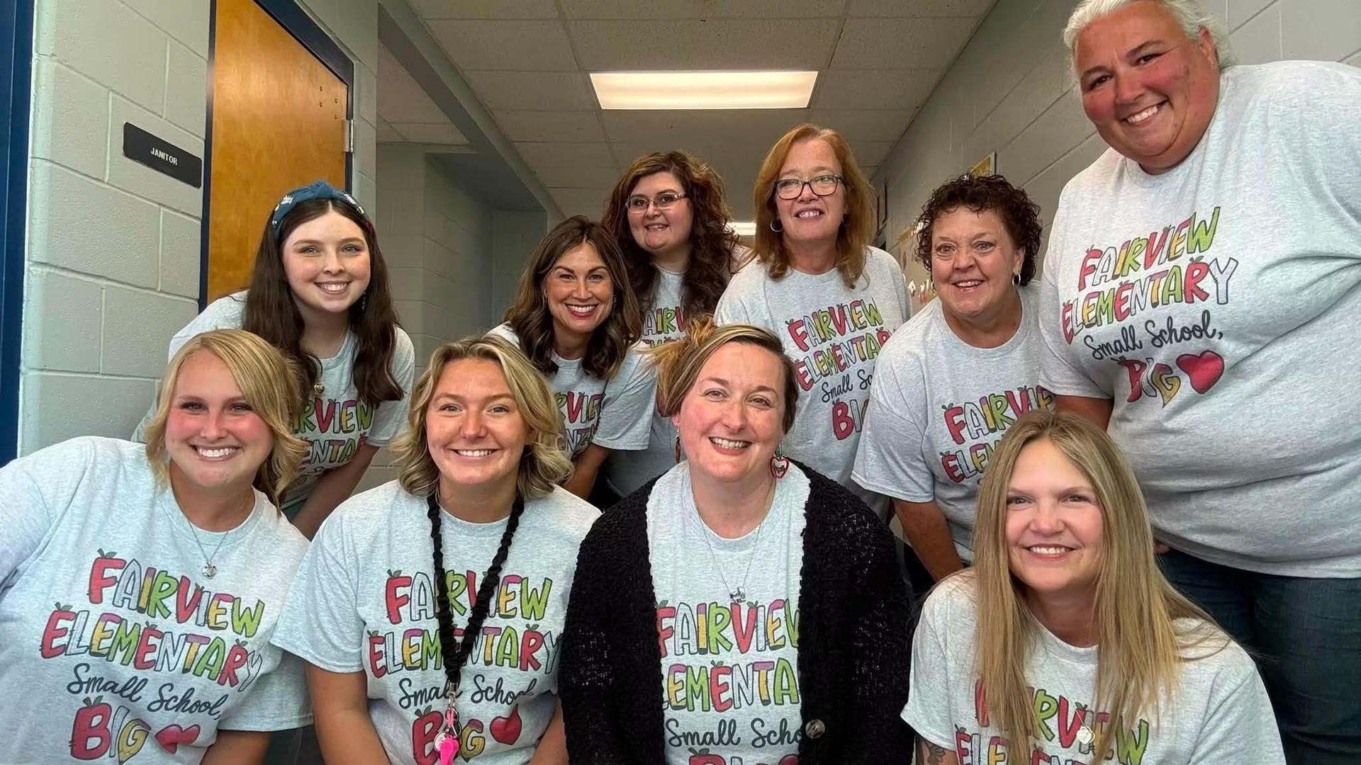 Group of educators in matching shirts smiling in a school hallway.