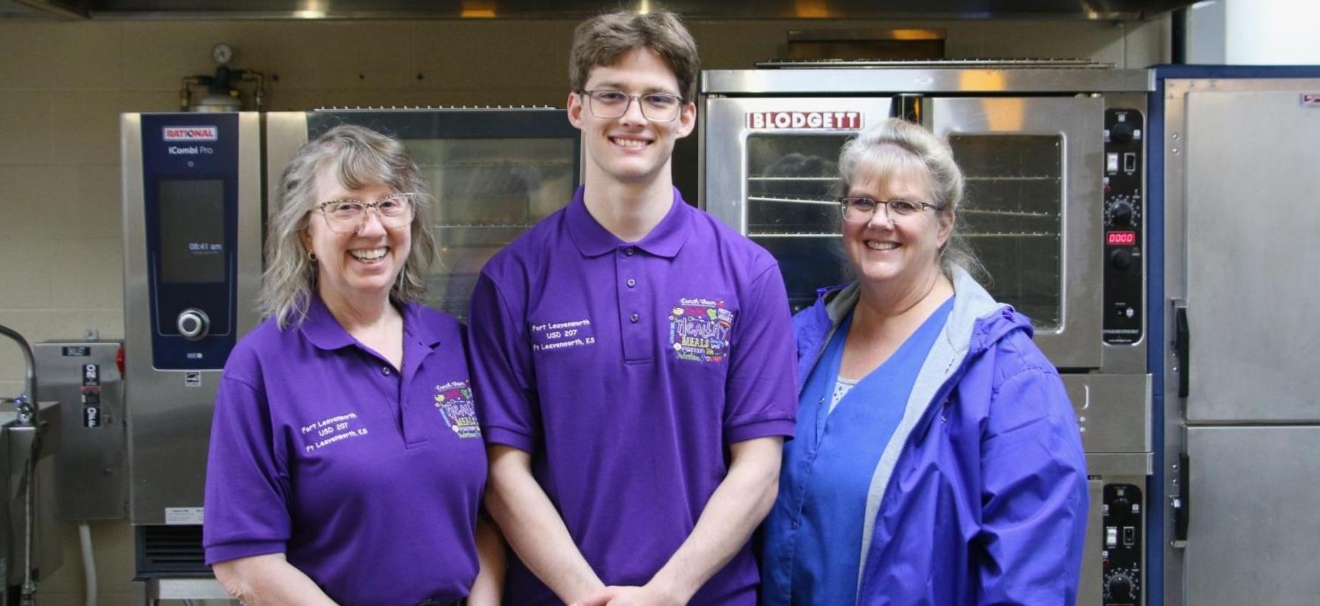 Three staff members, smiling, in a kitchen environment.