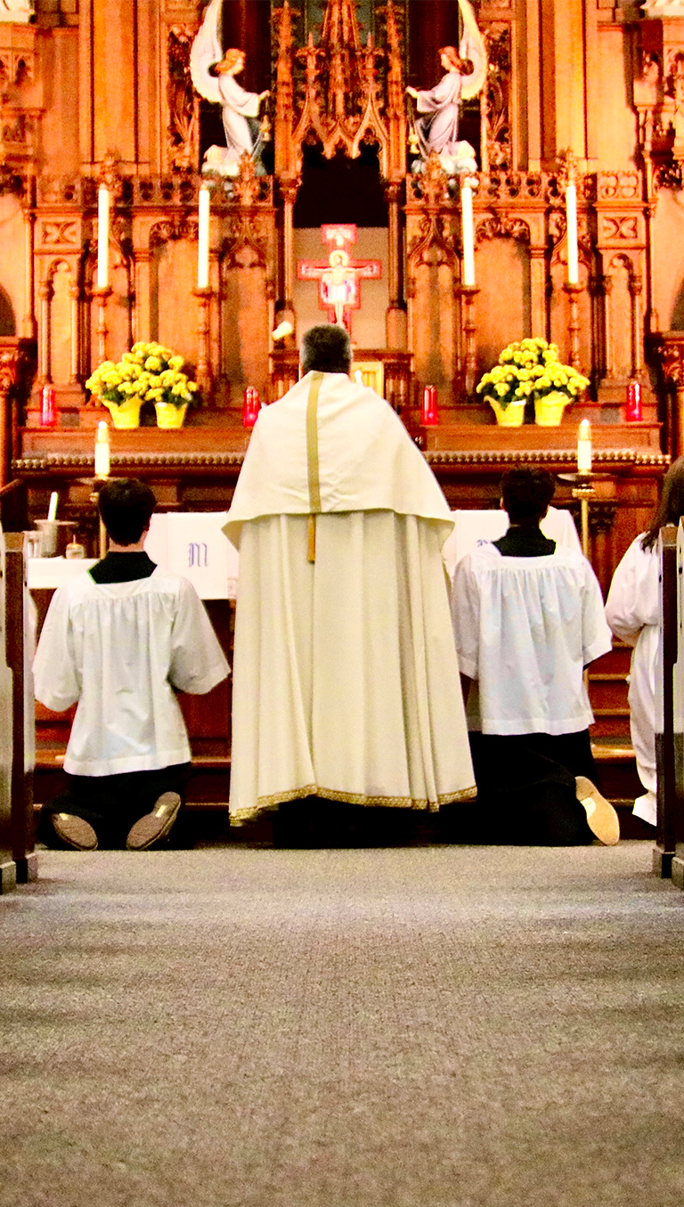 priest in white vestments faces the altar with altar boys genuflecting on either side