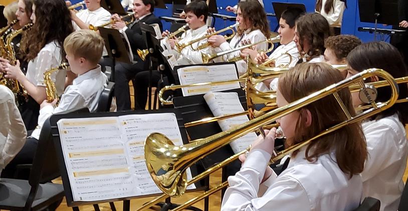 A band of musicians playing brass instruments during a concert in a school setting.