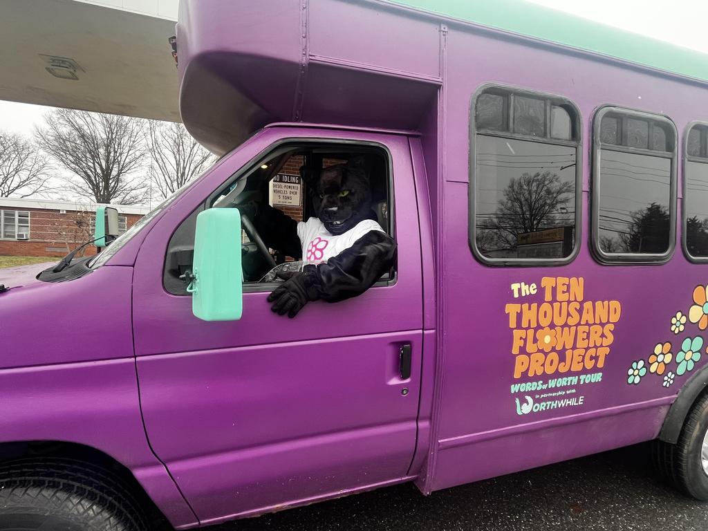 The Springfield Panthers mascot, Pawblo, sitting in the driver's seat of the Ten Thousand Flowers Project purple bus.