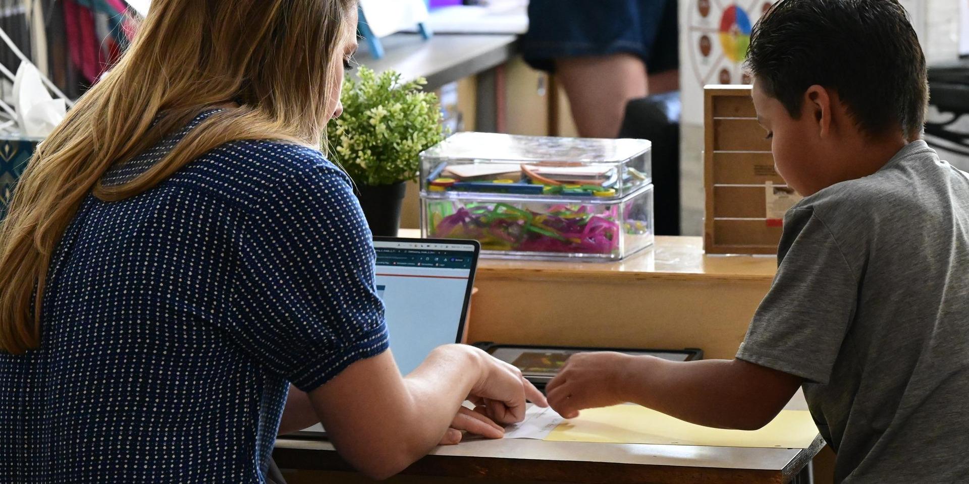 Teacher assisting a boy with a task at a table.