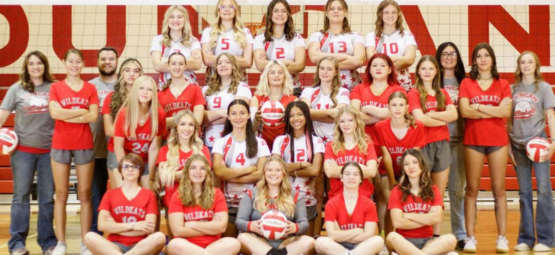 A large group of volleyball players in team uniforms posing together on a gym court.