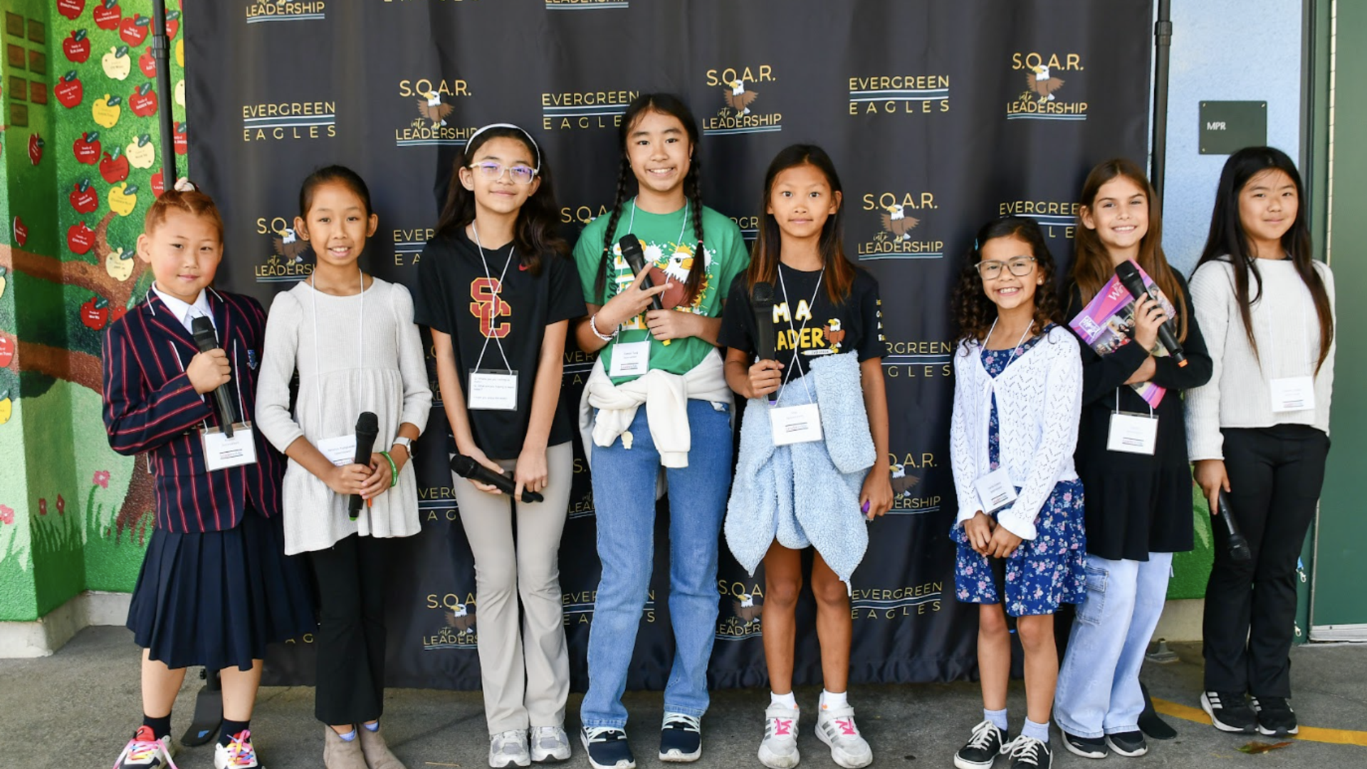 A group of eight girls standing together, smiling, against a backdrop.