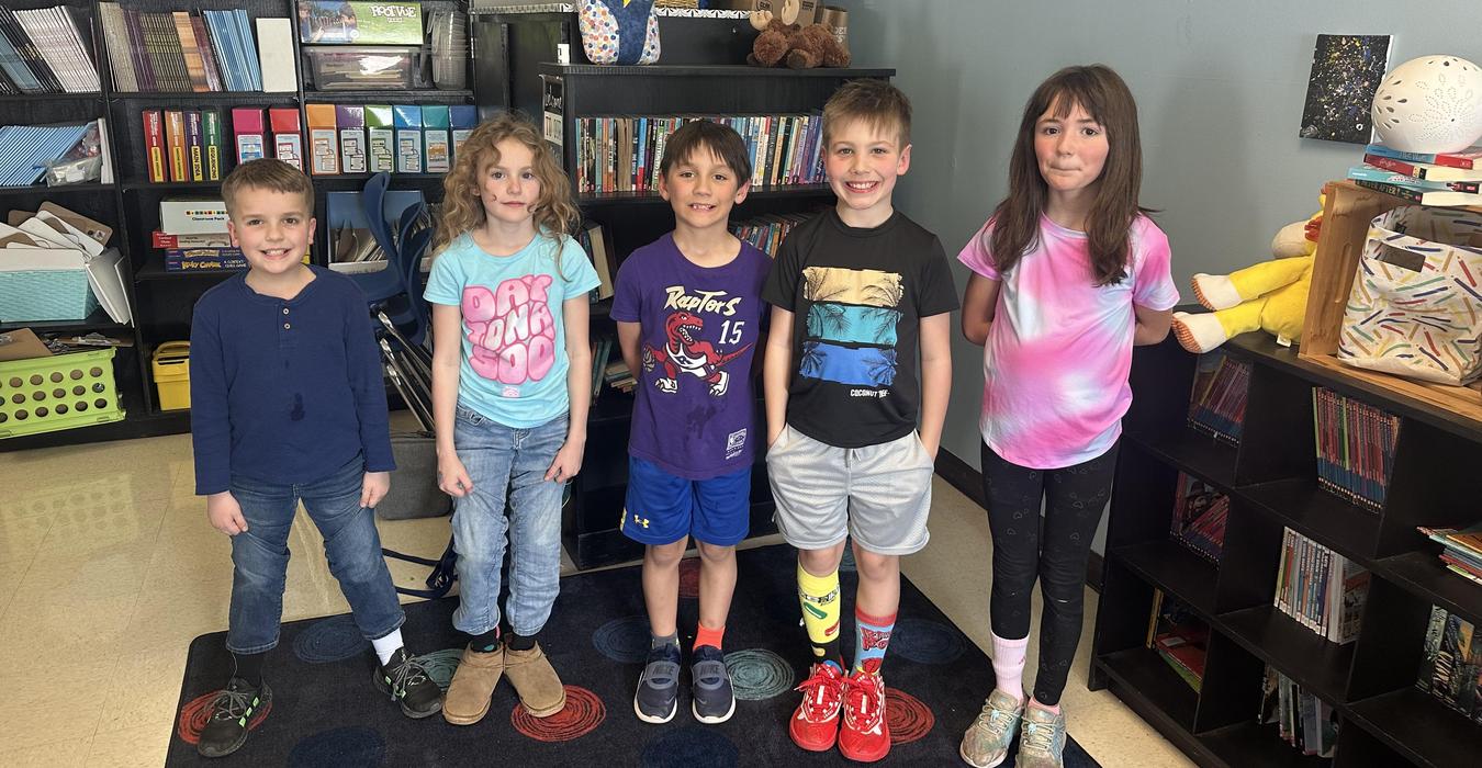 Five children standing in a classroom, each wearing colorful and mismatched socks.
