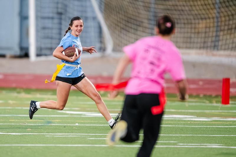 A high school student in a blue T-shirt runs with a football as a student in a pink shirt plays defense.