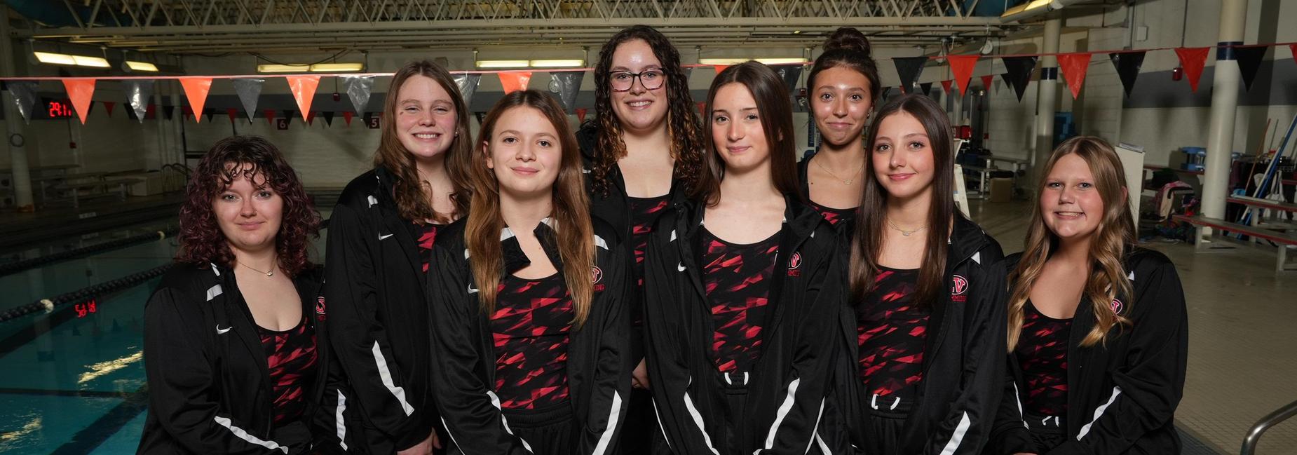 A group of nine female swimmers posing by a pool in athletic gear.