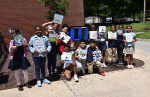 students holding books outside in front of little library
