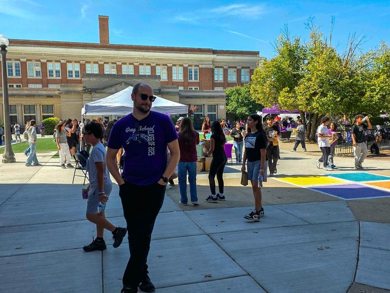 A busy outdoor school event with people mingling and colorful booths.