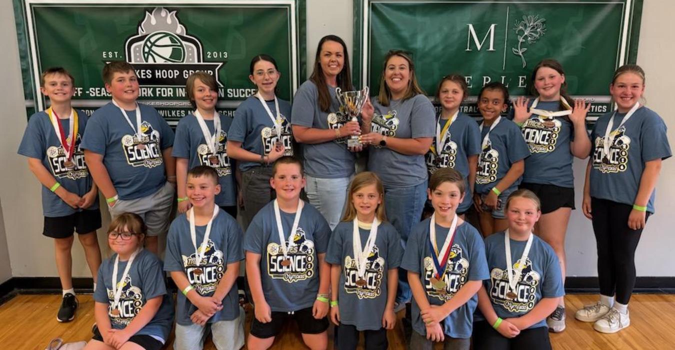Group of children and adults celebrating with a trophy in a gym.