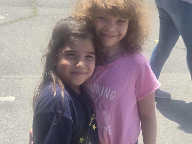 Two girls smiling and standing close together outdoors.