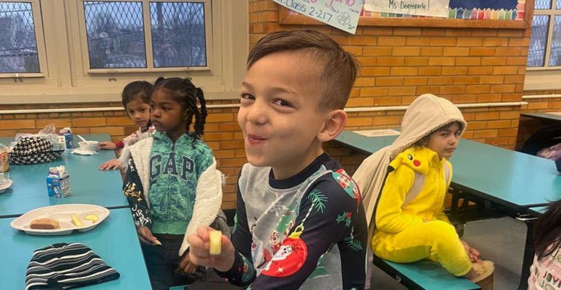 Smiling child in a colorful shirt enjoying lunch with classmates in a school cafeteria.