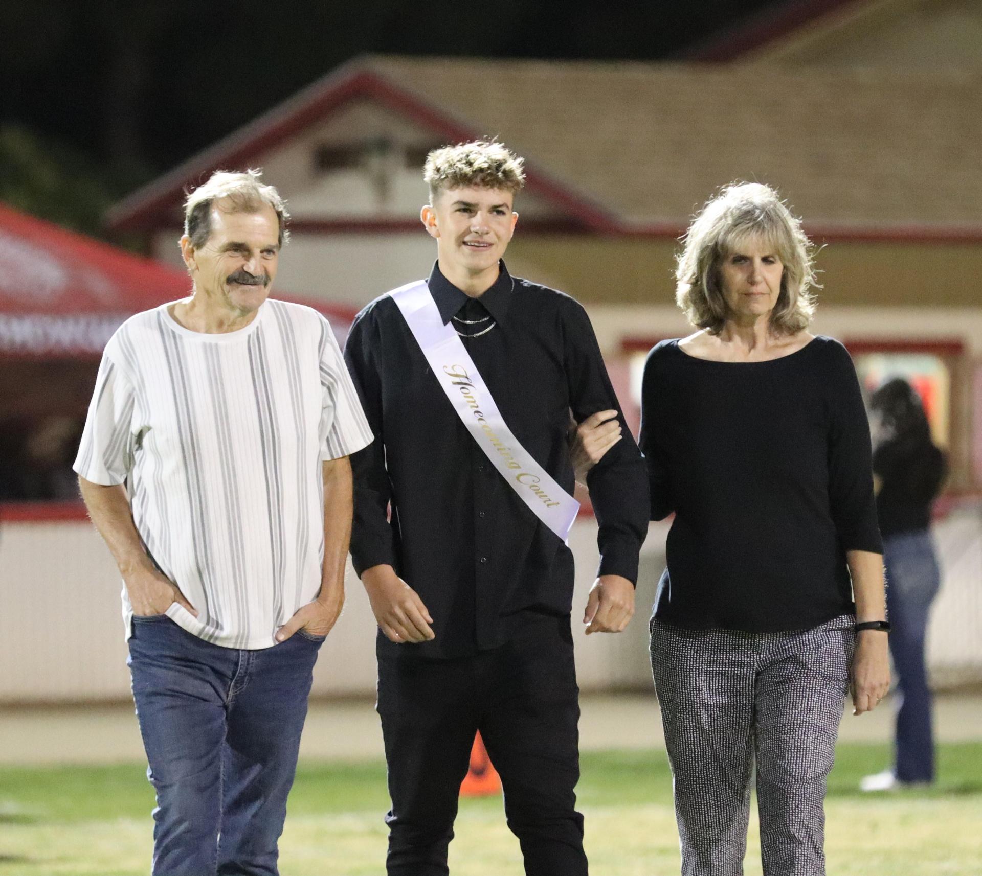 homecoming king and queen candidates walking across the field with their escorts