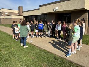 students in semicircle looking at sundial on the ground in front of them