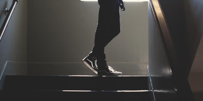 A person in black pants walking down dark stairs with a railing.