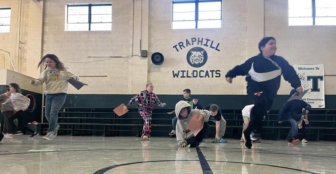 Children running and crawling in a gymnasium, collecting sheets of construction paper.