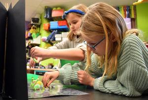 Two girls engaged in a craft activity, placing figures on a table.