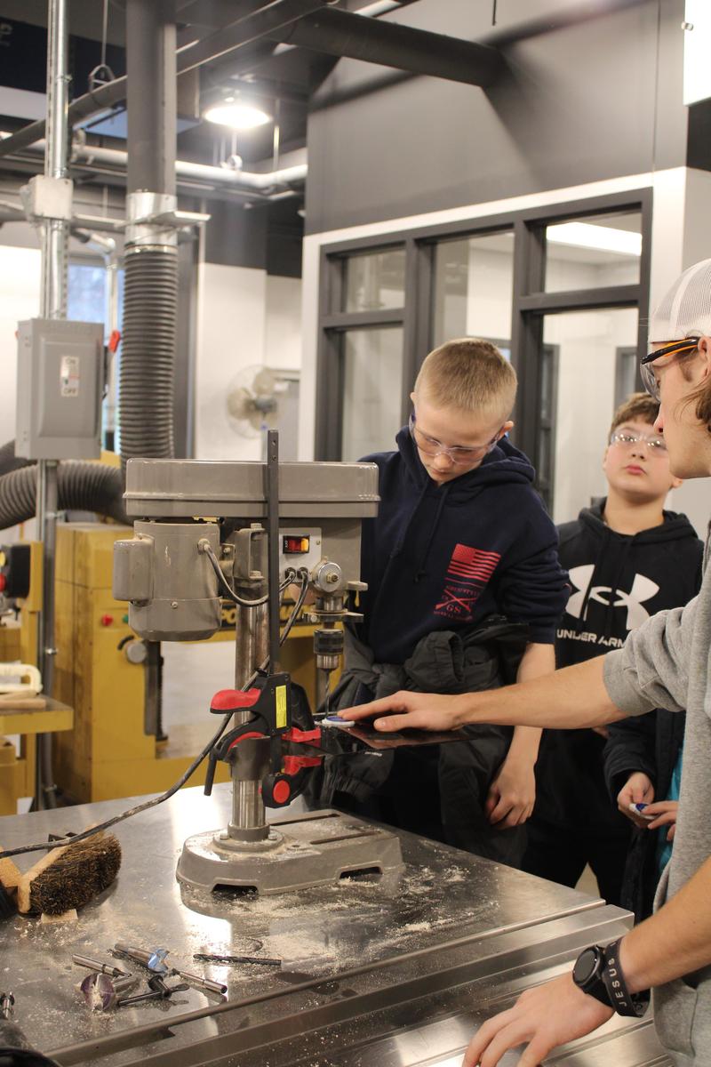 young student stands at drill press