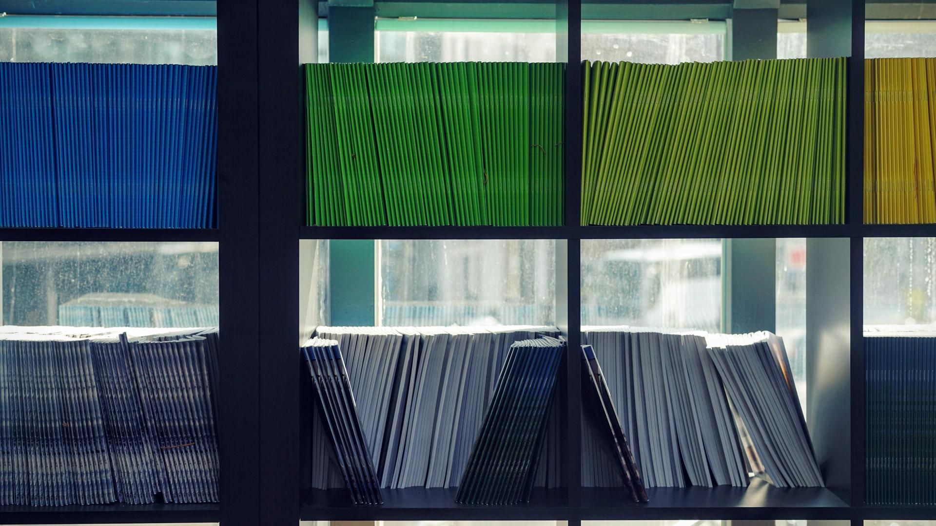 A bookshelf filled with various colored folders and books.