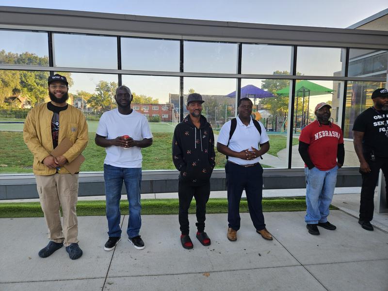 A group of fathers stand in front of the entrance to Mandela greeting scholars