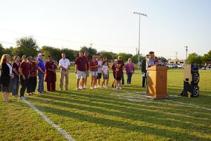 The Dusek family, board members, and district administrators gather on the field during the ceremony