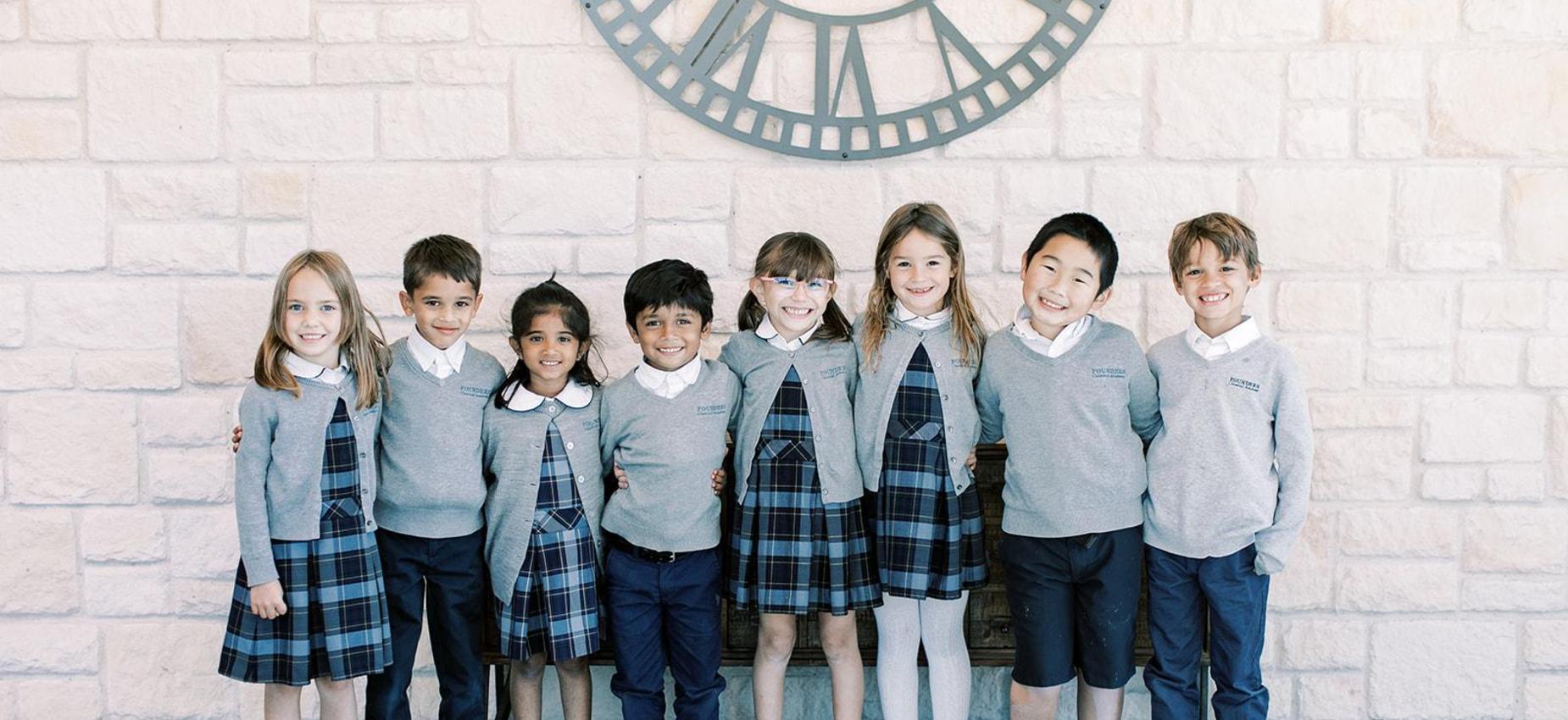 Elementary students in uniform stand in a row beneath a large clock