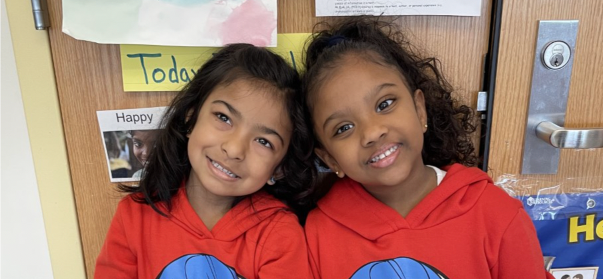 Two smiling girls in matching red hoodies with cartoon designs.