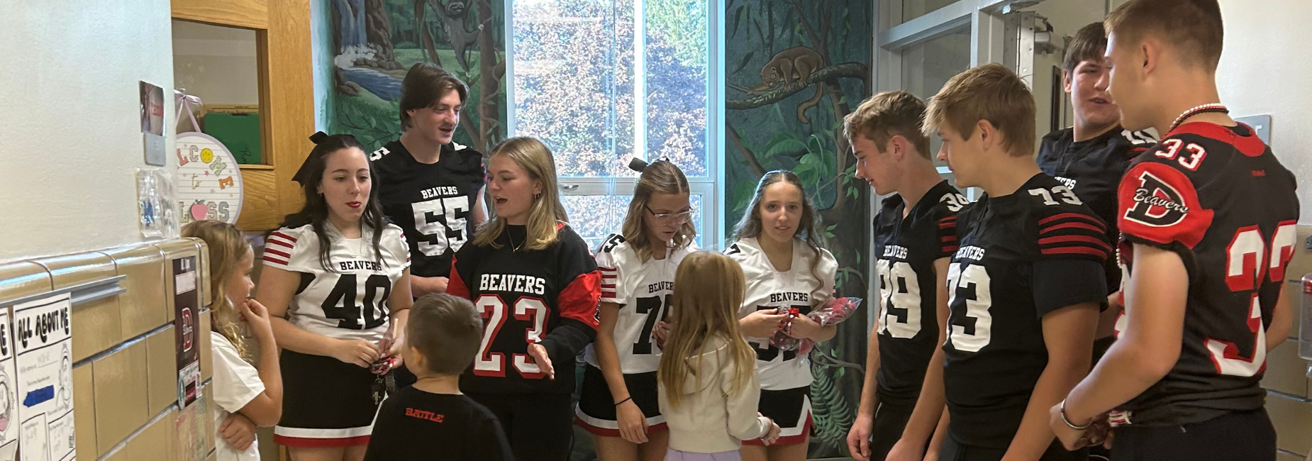 Students in football jerseys interacting with younger kids in a hallway.