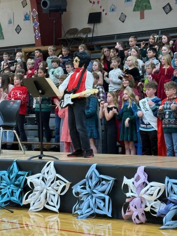 A performer in costume playing guitar on stage with a group of children behind him.