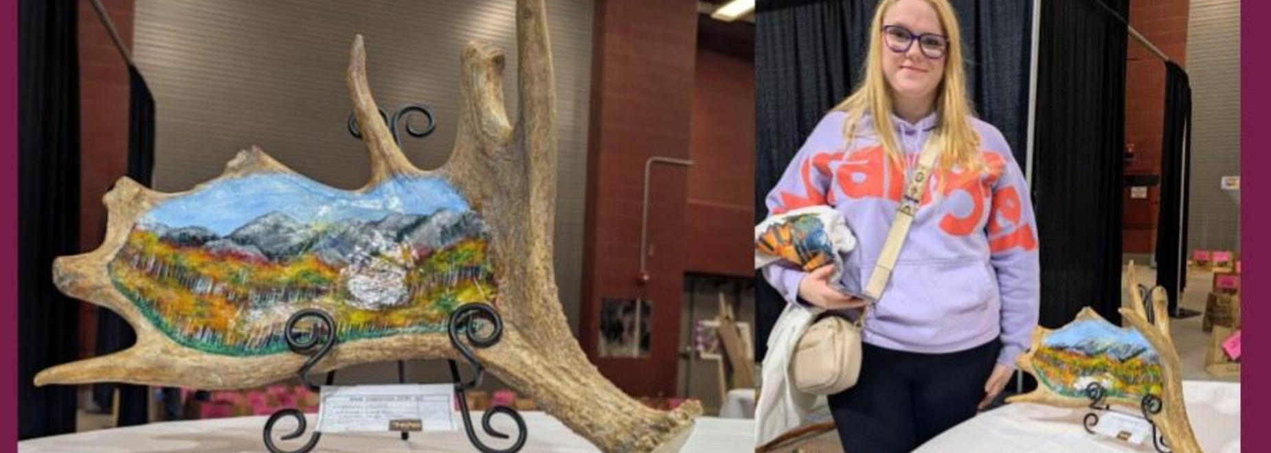 A young woman with glasses alongside a painted wooden art piece in an indoor venue.