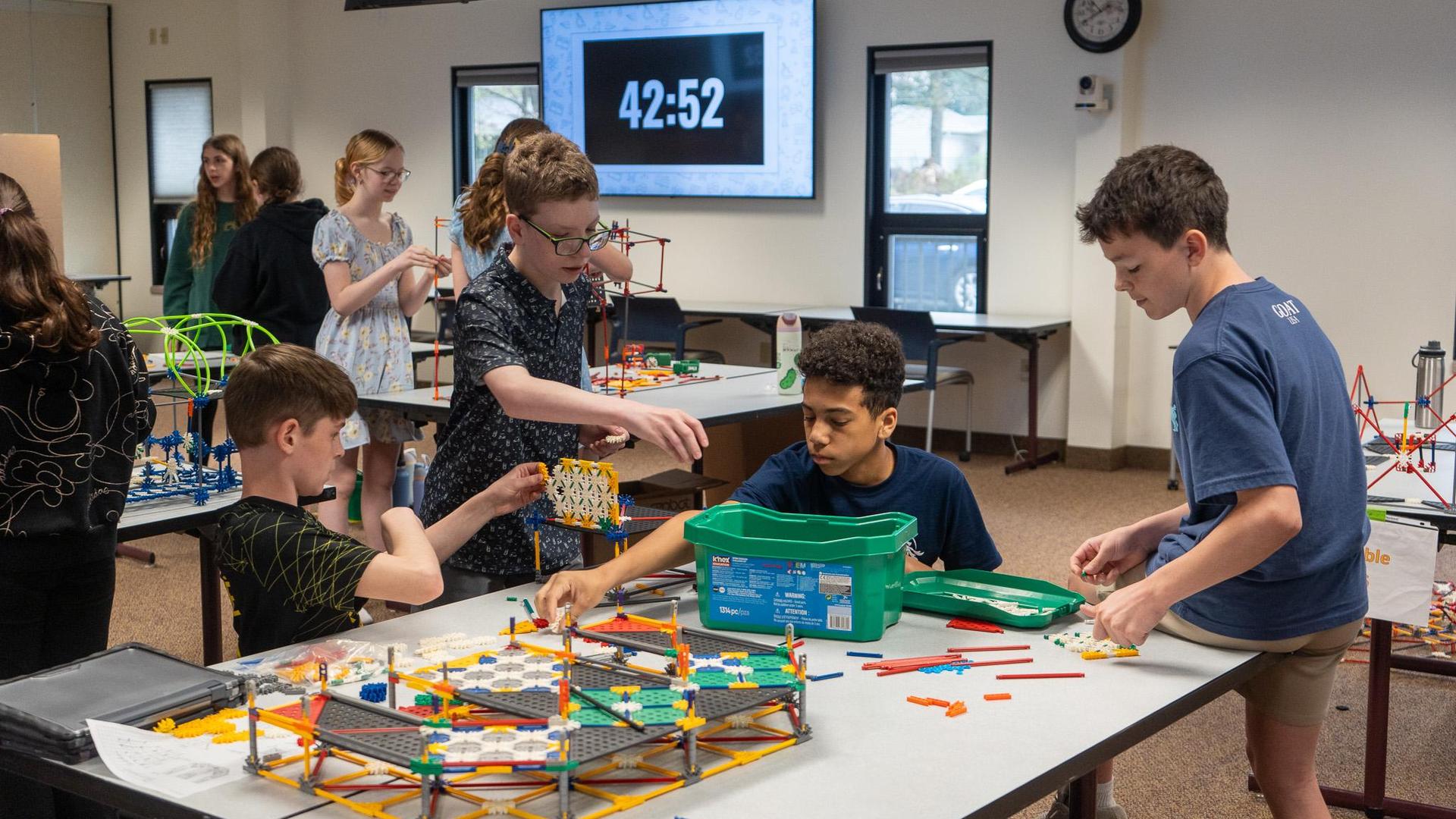 Four middle school students work collaboratively building a model out of colorful K'nex, as the timer in the background ticks down with 42 minutes left to build, during a K'Nex STEM Design Challenge.