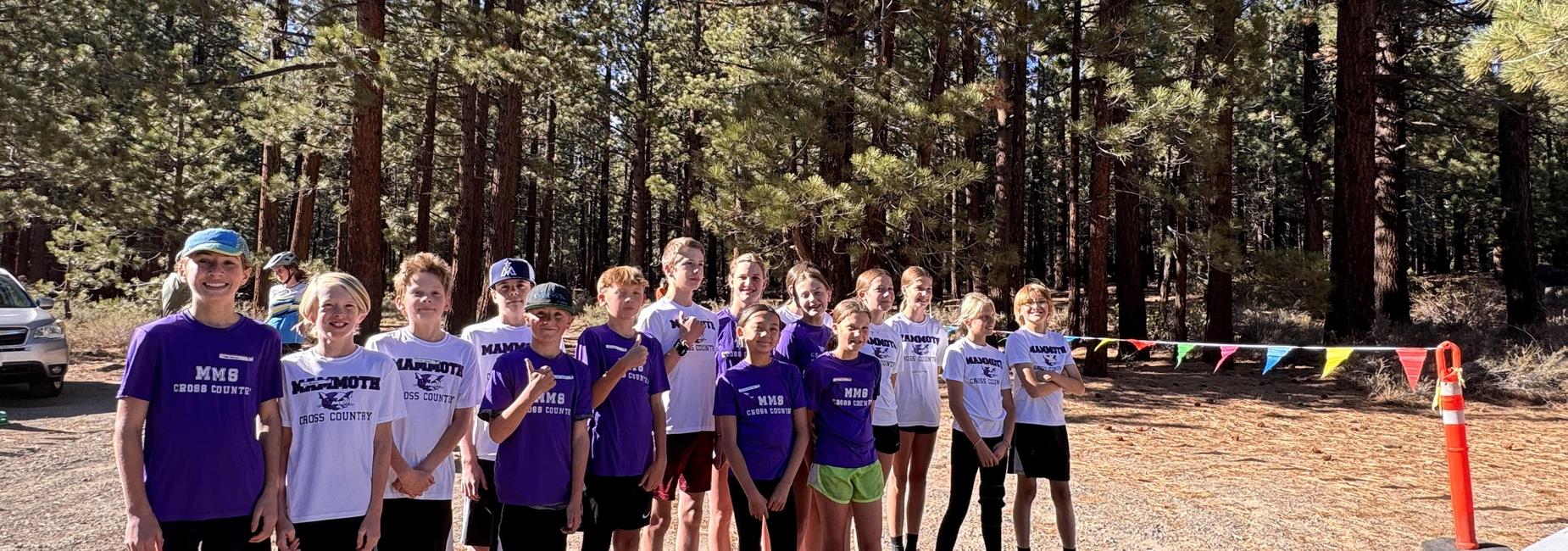 A group of young runners in athletic gear posing in a forest during a cross country event.