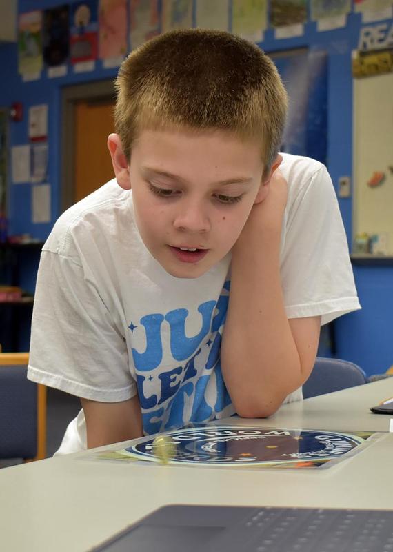 Boy in a white shirt looks intently at a game on a table.