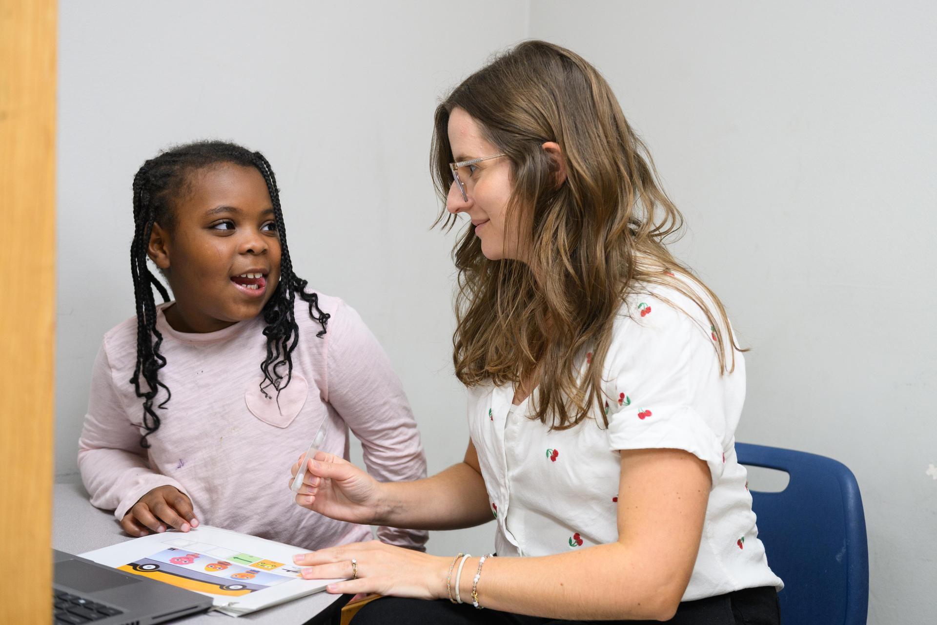 Student on left wearing pink shirt is smiling at teacher on right.