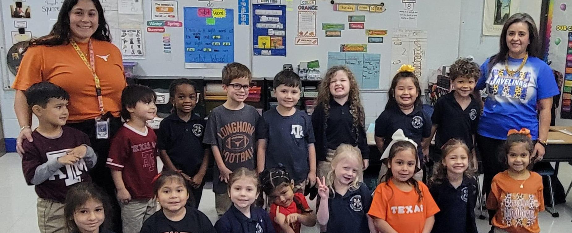 A group of smiling children in matching shirts posing for a photo in a classroom.