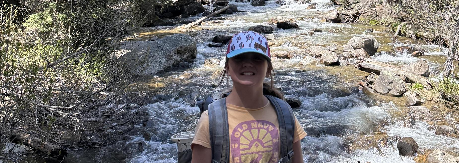 Individual with a colorful hat stands before a waterfall and river.