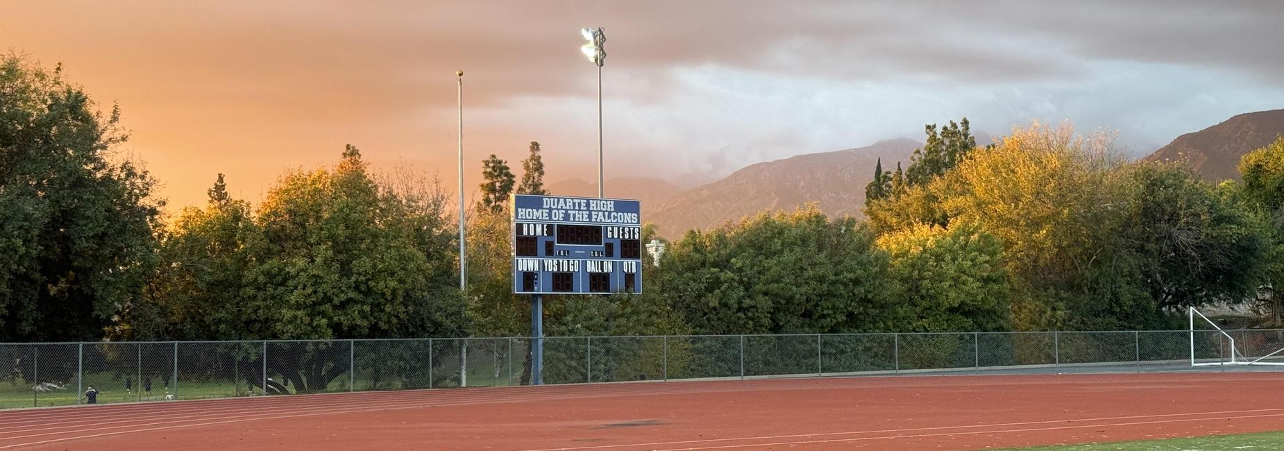 Empty athletic track with a scoreboard and trees against an evening sky.