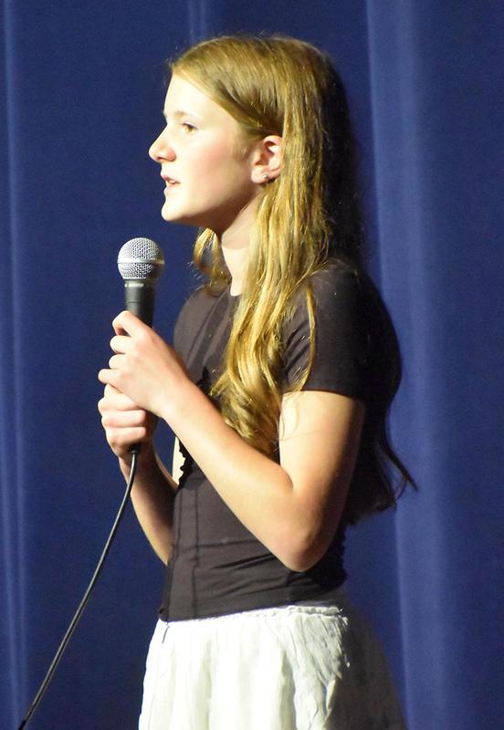 Girl with long hair speaking into a microphone, wearing a black shirt.