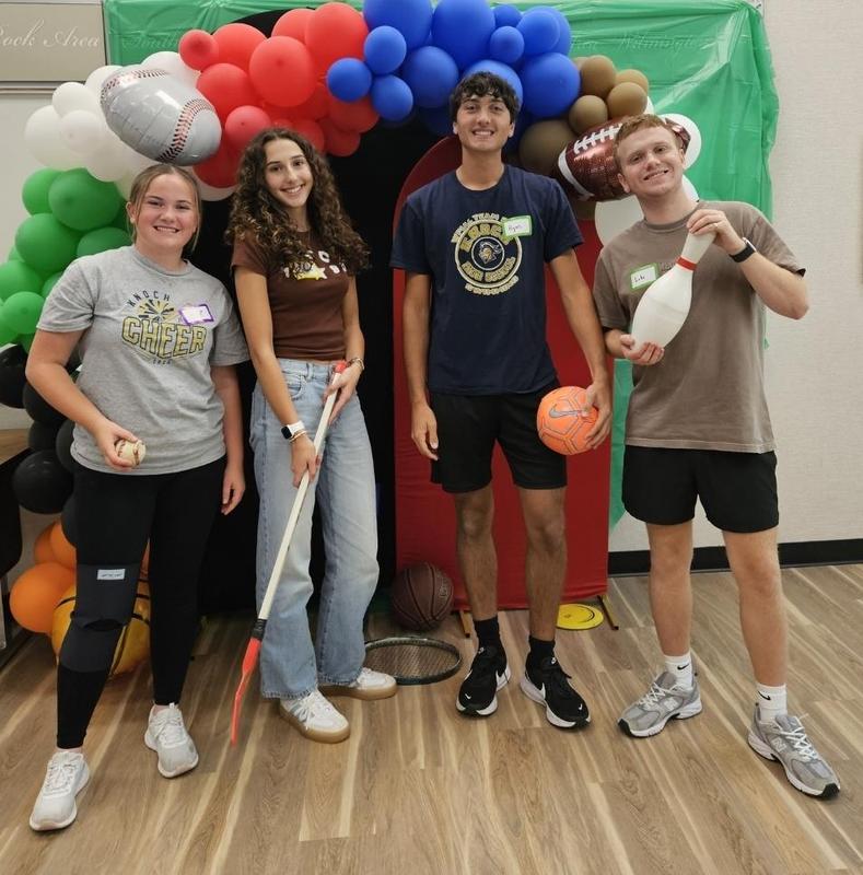 four teenagers standing by a balloon arch