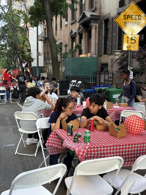 Children eating at tables with checkered tablecloths outdoors.
