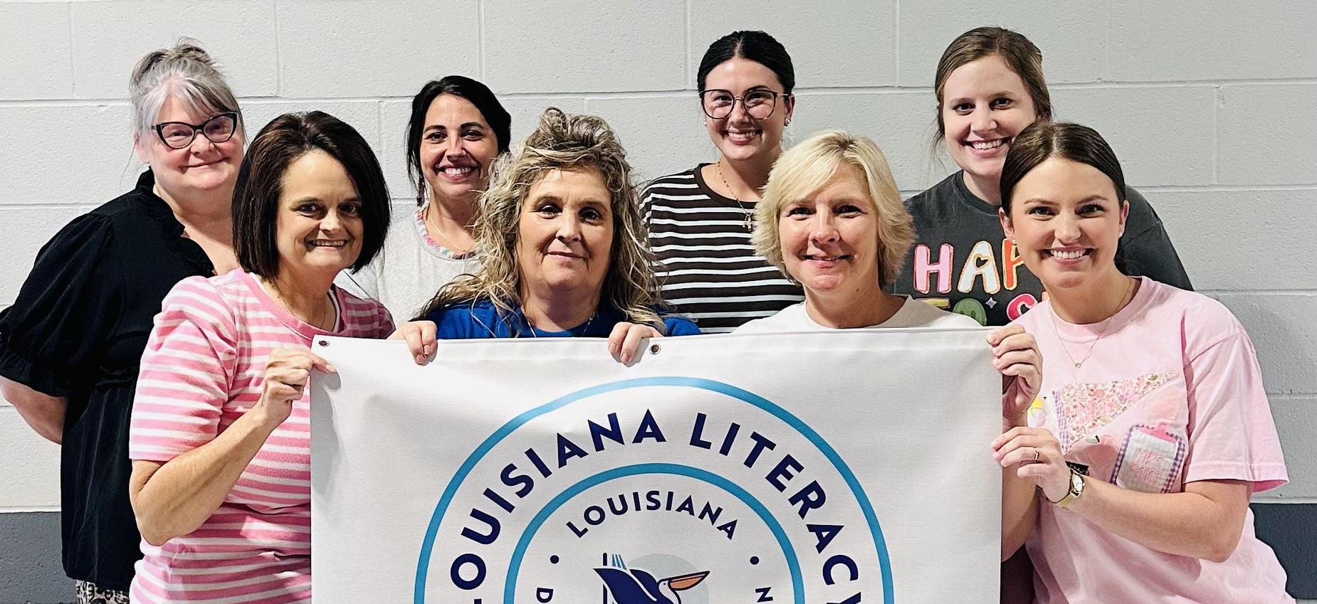 Four women holding a banner for Louisiana literacy leader recognition with a logo.