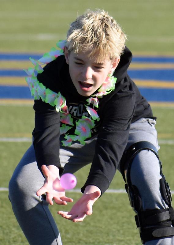 Boy in a lei lunges to catch a balloon at a sports field.