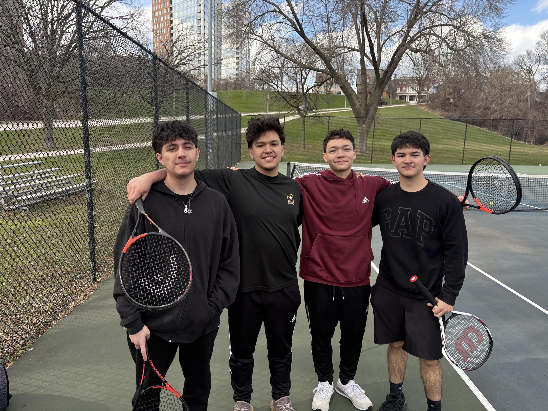 Four tennis players smiling together at practice.