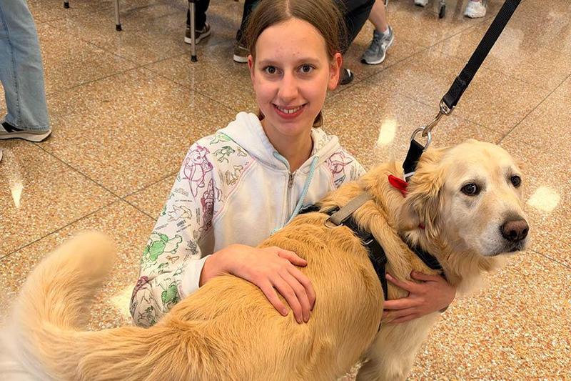a girl kneels on a cafeteria floor with a dog