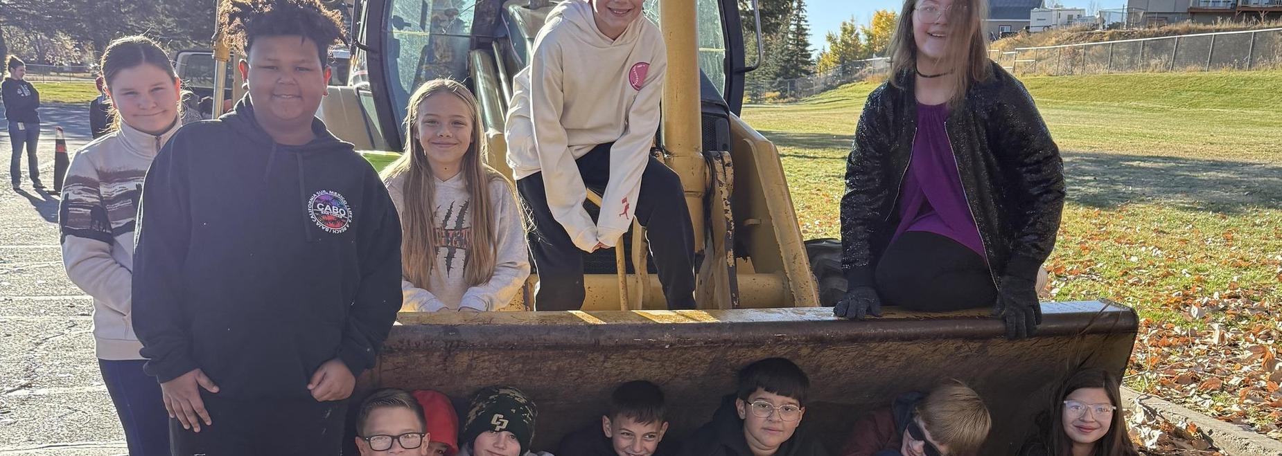 Group of children sitting together in a large machinery bucket outdoors.
