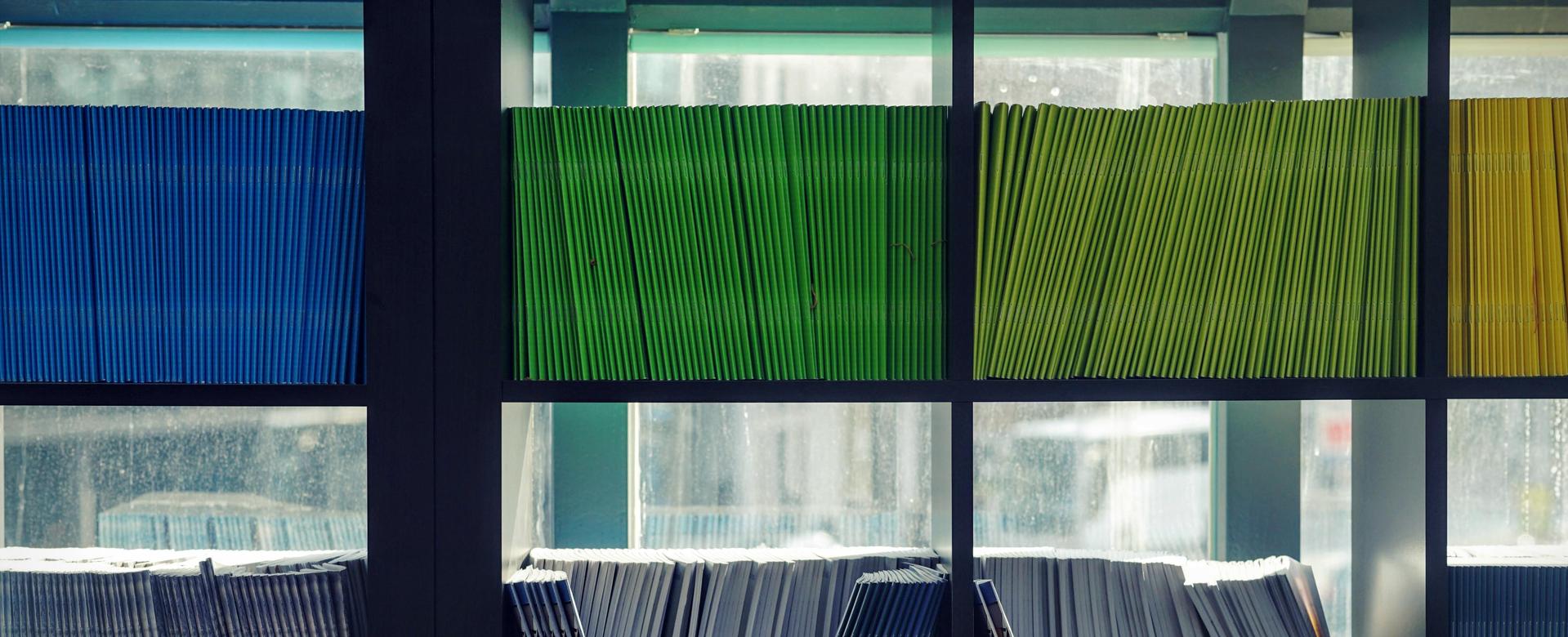 A bookshelf filled with various colored folders and books.