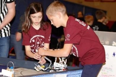 boy and girl in maroon shirt work on robot on a table