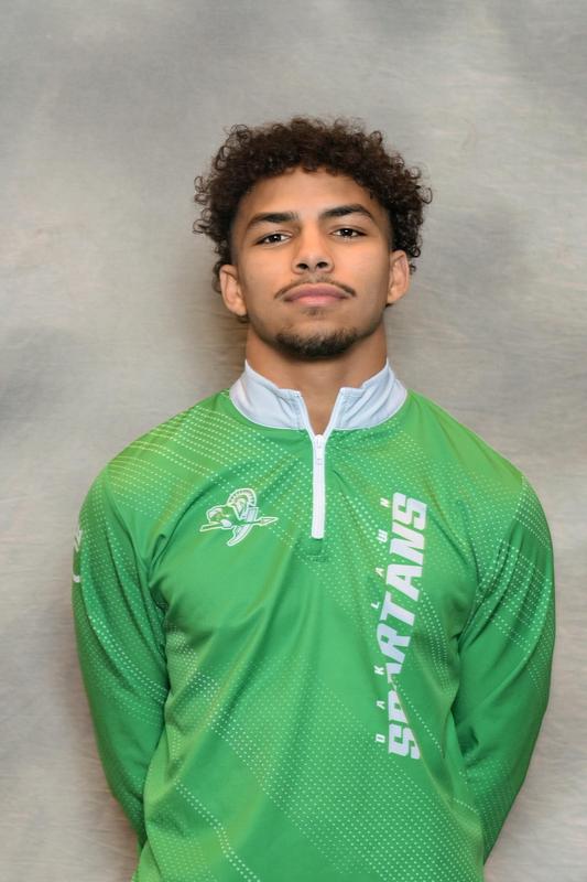 male athlete in green athletic jacket poses with grey backdrop