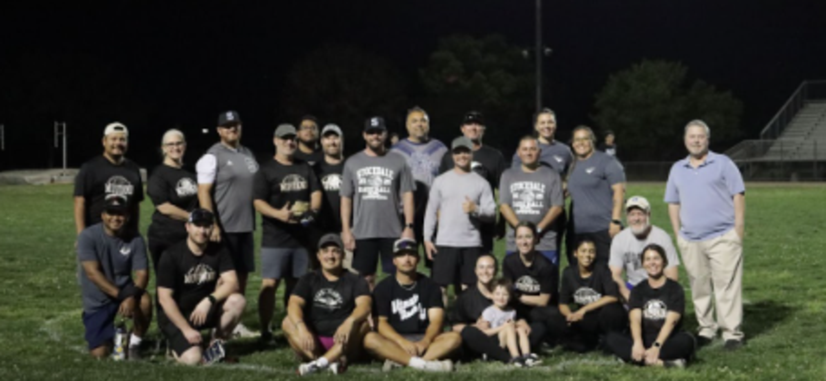 A large group of people gathered on a field, posing for a team photo at night.