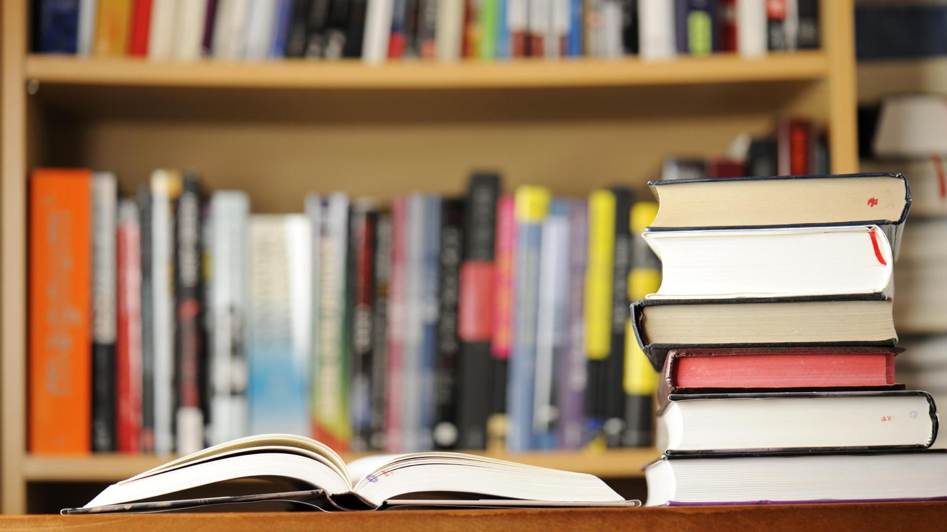 An open book in front of a stack of closed books on a wooden surface.